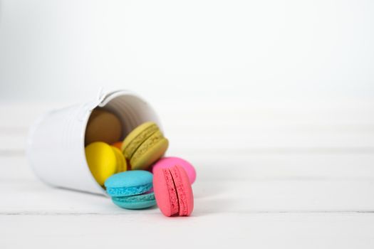 Macaroons and flowers on the white wooden background.