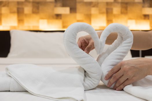 Close-up of hands putting folded swans bird of fresh white bath towels on the bed sheet in the hotel.