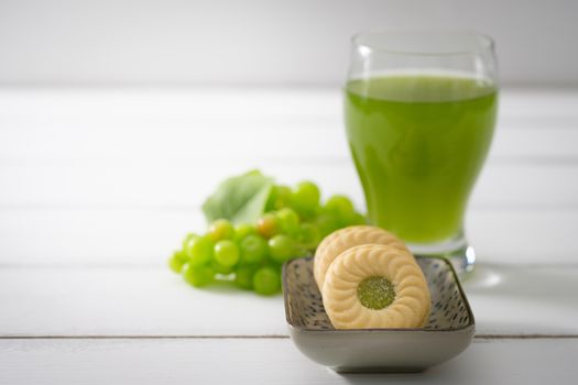 Biscuits put on a ceramic plate and green grapes placed close together on white wooden background, Selective focus.