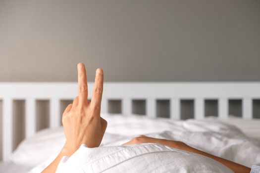 Woman raising two fingers up on hand on the bed show that you should welcome the new morning.
