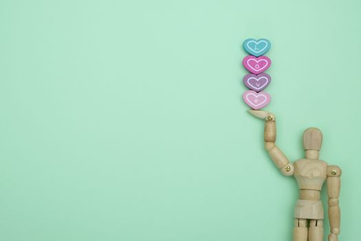 Wooden dummy holding a heart-shaped  on green background with copy space for write and valentine concept.
