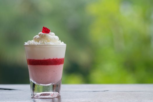Strawberry mousse cake in a small glass placed on a wooden table in bokeh background with copy space.