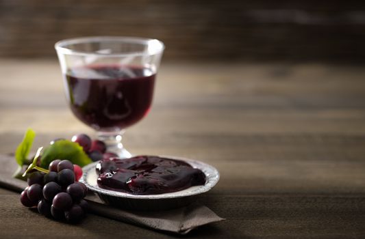 A glass of grape juice, bunch of grapes and blueberry pie on brown wooden background, Selective focus, Dark image tone.
