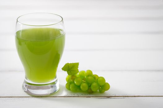 A glass of grape juice and bunch of green grapes on white wooden background, Selective focus.
