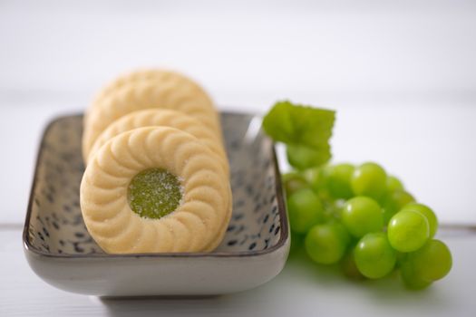 Biscuits put on a ceramic plate and green grapes placed close together on white wooden background, Selective focus.