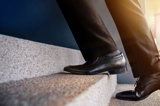 Motivation and challenging Career Concept. Steps Forward into a Success. Low Section of Businessman Walking Up on Staircase. Male in Black Formal Dress