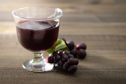 A glass of grape juice and bunch of grapes on brown wooden background, Selective focus, Dark image tone.