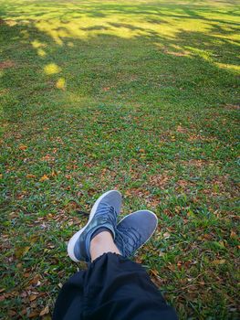 Woman's legs in grey shoes sit on dry leaves in the park.