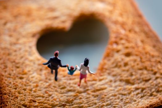 Love Concept. Miniature of Happy Family Walking on Burned Sliced Toasted Bread with a shape of Heart