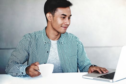 Happy Young Businessman Working on Computer Laptop in Office. Smiling and looking at Computer