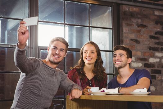 Smiling friends having coffee and taking selfies at coffee shop