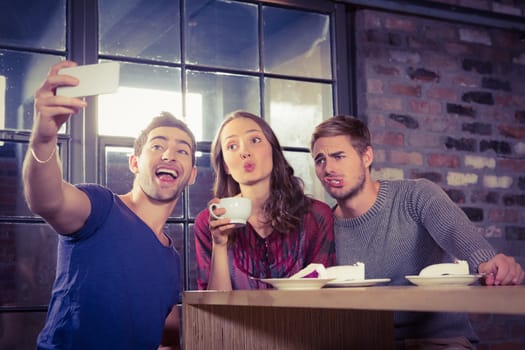 Grimacing friends taking selfies at coffee shop