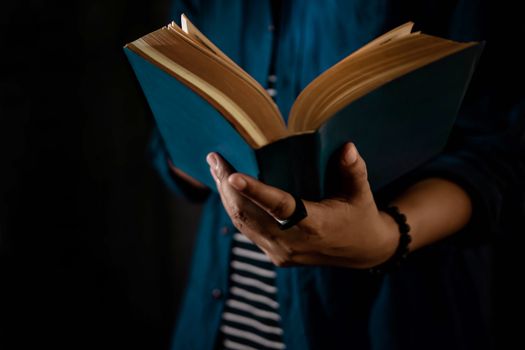 Reading Concept. Person Holding Opened Bible Book on Hand. Dark Tone, Cropped image