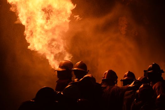 firefighters with fire hose fight with fire at night