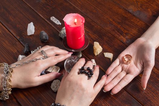 A Gypsy woman performs a love spell. A clairvoyant palmist reads by hand with a candle. A fortune teller predicts the fate of love with wedding rings, a magic ball, lighted candles and magic stones.