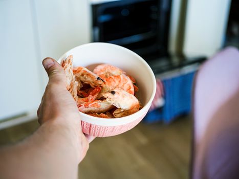 Bowl filled with fresh shrimps in man hands. Chairs are visible in the blurred background. Food for diet - Grilled shrimps with mango salad. Home cook in Asian kitchen.