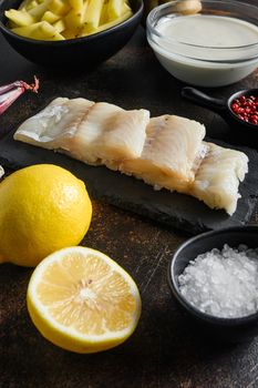 British traditional fish and potato chips ingredients raw fish fillet, beer batter, potatoe, shallotgarlic, salt, peppercorns on rustic metal textured surface or table side view .