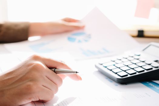 Close up of businessman or accountant hand holding pen working on calculator to calculate business data, accountancy document and laptop computer at office, business concept