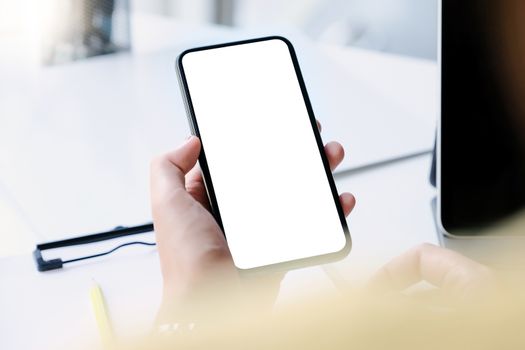 Woman hand holding smartphone on workplace. Blank screen mobile phone for graphic display montage.