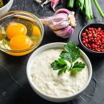 Organic lemon ranch dressing in a small jar with fresh greens. Tartar sauce. Making sauce from capers, cucumbers, parsley, lemon and eggs. For fish and chips and sea food Square on black stone surface.