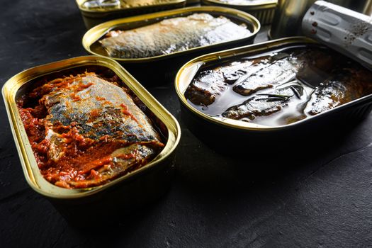 Saury, mackerel, sprats, sardines, pilchard, squid, tuna, Canned fish in tin cans. Open and closed over black slate background side view new wide angle.