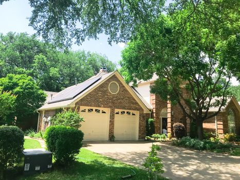 Front porch entrance of typical residential house in suburban Dallas, Texas, America with solar panel on shingle roof surrounds by tall oak and pine trees.