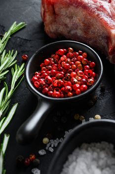 Rose Peppercorn and Rosemary herbs close up on black stone table with spices and raw meat near side view selective focus vertical