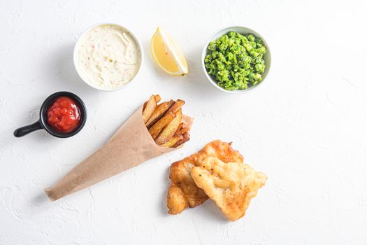 Components of traditional british set of fish and chips beer battered cod fillet, fries , lemon slices, tartar sauce and mushy peas , tomato ketcup for choice over white concrete background top view space for text