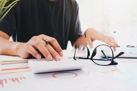 Close up Business man using calculator and laptop for do math finance on wooden desk in office and business working background, tax, accounting, statistics and analytic research concept