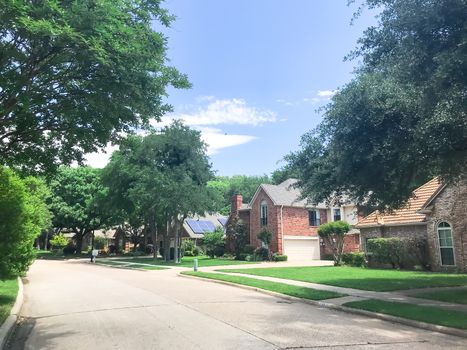 Green lush residential neighborhood in suburbs Dallas, Texas, America. Row of upscale house with solar panel roof and mature trees.