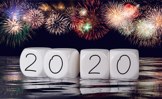 Multiple firework explosions against dark blue sky with calendar date and water reflections for 2020 New Years celebrations