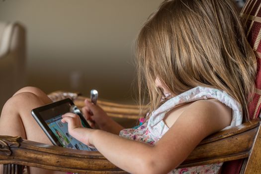 Young toddler lying on chair and playing games on an electronic tablet device
