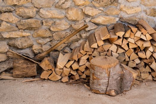 Chopped wood and axe stacked against the stone wall of a rustic farmhouse