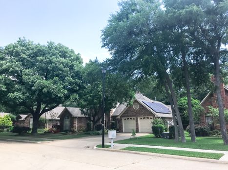 Front porch entrance of typical residential house in suburban Dallas, Texas, America with solar panel on shingle roof surrounds by tall oak and pine trees.