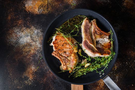 Grilled organic pork steak with herbs on bone in grill frying pan hot with smoke and hot oil just from fire, top view cooking bone with seasonings rustic metal background.