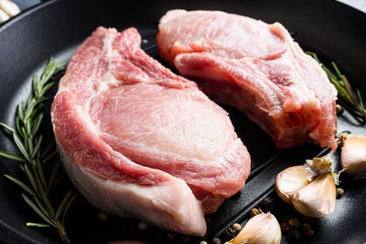 Raw gourmet pork cutlet for grill in frying pan black skillet with herbs, spices close up.