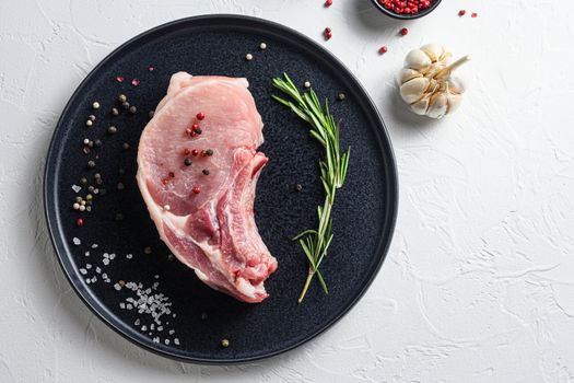 Fresh pork steak in a black round plate on a white stone background with rosemary garlic peppercorns ingredients for grill top view space for text.