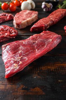 Alternative Flank bavette or flap steak beef t steak near tri-tip and top blade oyster cuts close up in front of other cuts in butchery on old wood table side view vertical.