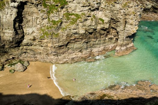 Two small girls and dog playing on beach and in sea near Tintagel, Cornwall, England, UK