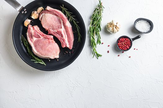 Fresh pork steak in a frying grill pann on a white stone surface with rosemary garlic peppercorns ingredients for grill top view side for text concept.