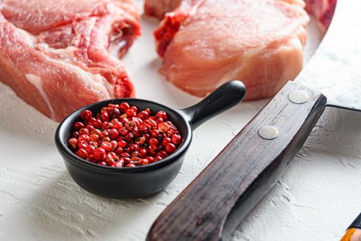 Rose peppercorns in black ceramic bowl overFresh organic raw pork meat set for grilling, baking or frying and ingredients for cooking on white surface side view