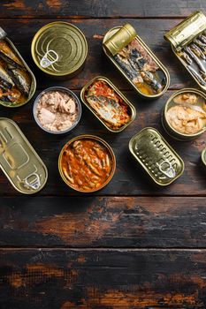Tin cans for fish with different types of seafood, opened and closed cans with Saury, mackerel, sprats, sardines, pilchard, squid, tuna, over dark wood old table flatlay top view space for text.