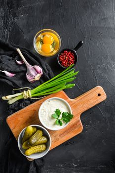 Tartar Sauce with organic ingredients pickles, capers, dill, parsley, garlic, lemon and mustard rose peppercorns on a dark black stone concrete background. Horizontal, top view vertical.