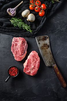 Raw top blade cut organic meat with vegetable rosemary and other ingredients for bbq or gtrill top view over black stone background vertical .