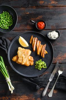 Fish chips with dip and lemon black plate with British traditional cusine food with beer-battered cod and fries and a side of tartar sauce mushy minty peas served in the Pub or Restaurant.