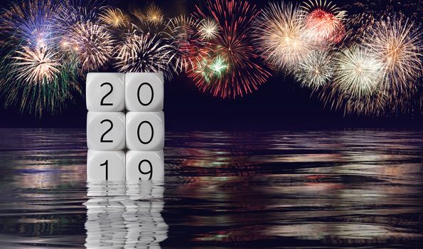 Calendar blocks showing 2019 sinking into the ocean as 2020 starts with fireworks in the background