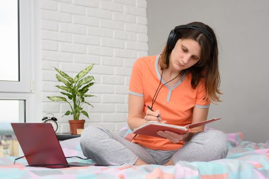 Girl student at home writes online lecture materials in a notebook