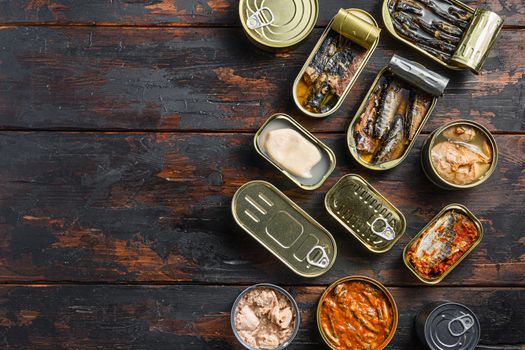Tin cans for fish with different types of seafood, opened and closed cans with Saury, mackerel, sprats, sardines, pilchard, squid, tuna, over dark wood old table flat lay top view space for text.