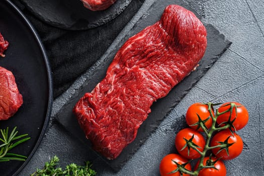 Raw tri tip cut black angus organic steak on a black plate and stone slate with seasonings, herbs grey concrete background. Top view close up