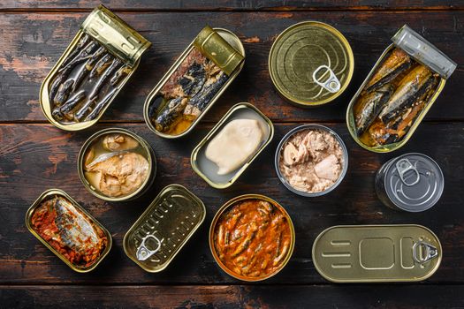 Tin cans for fish with different types of seafood, opened and closed cans with Saury, mackerel, sprats, sardines, pilchard, squid, tuna, over dark wood old table flatlay top view .